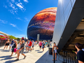 Enhanced artwork of the Las Vegas Sphere with a cosmic display, blue sky and plaza visitors